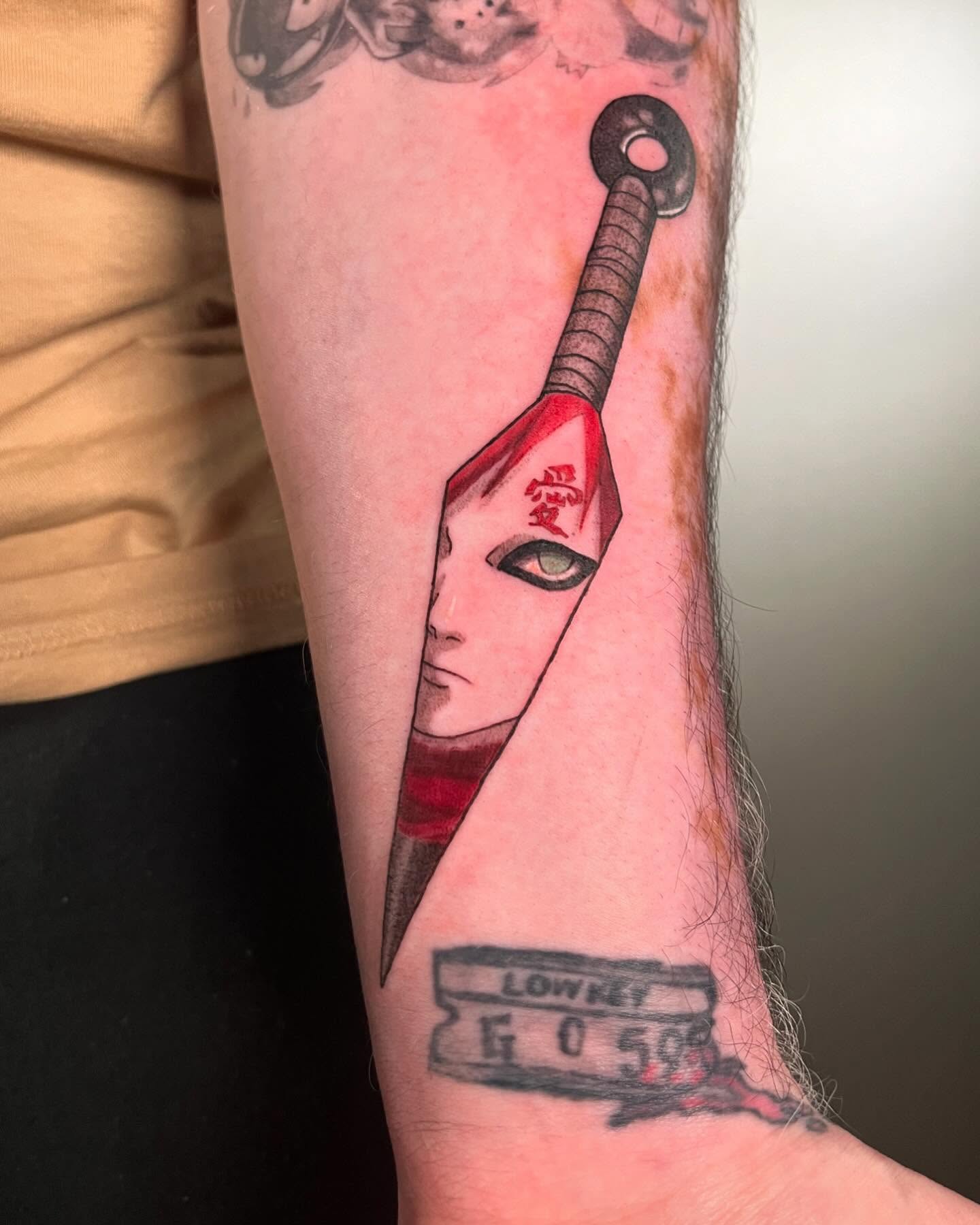 Tatuagem do Gaara com lâmina e rosto do personagem no braço